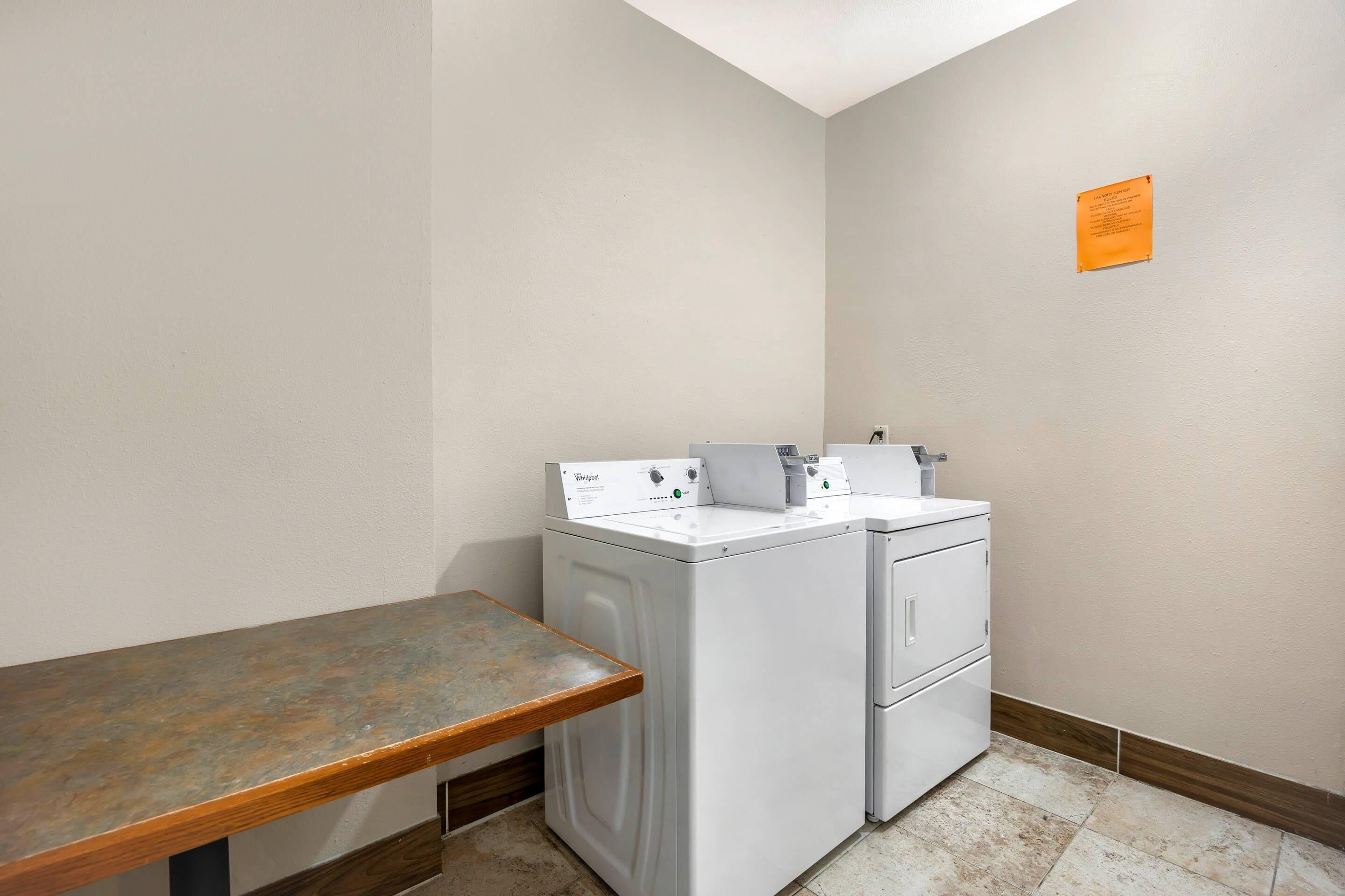 A laundry room with a washing machine and dryer, a wooden bench, and a small orange sign on the wall.