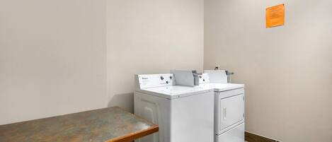 Une buanderie équipée d’un lave-linge et d’un sèche-linge, d’un banc en bois et d’un petit panneau orange accroché au mur.