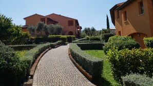 A paved pathway leading to a building with a tiled roof and a garden with neatly trimmed hedges. - Borgo Etrusco S.p.A. (Scarlino)