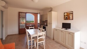 A compact kitchen with a dining area, a TV on a cabinet, and a view through an open door. - Borgo Etrusco S.p.A. (Scarlino)