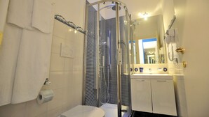 Un baño con ducha envuelta en vidrio, inodoro y lavamanos con espejo.