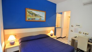 Una habitación de hotel con cama, lámparas de noche, escritorio y un cuadro en la pared.