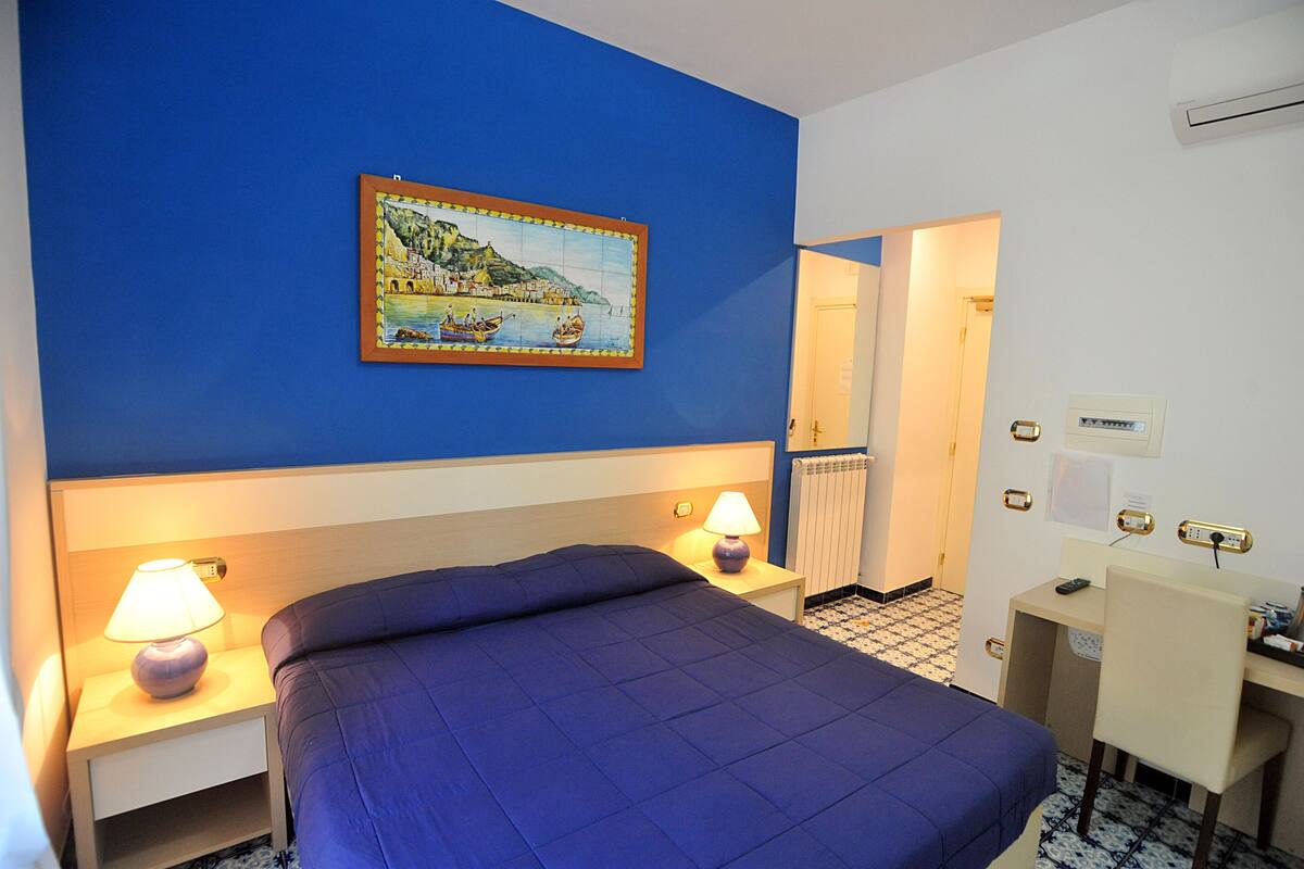 Ein Hotelzimmer mit Bett, Nachttischlampen, Schreibtisch und einem Bild an der Wand.