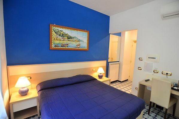 A hotel room with a bed, bedside lamps, a desk, and a painting on the wall. - Villa Adriana B&B (Amalfi)