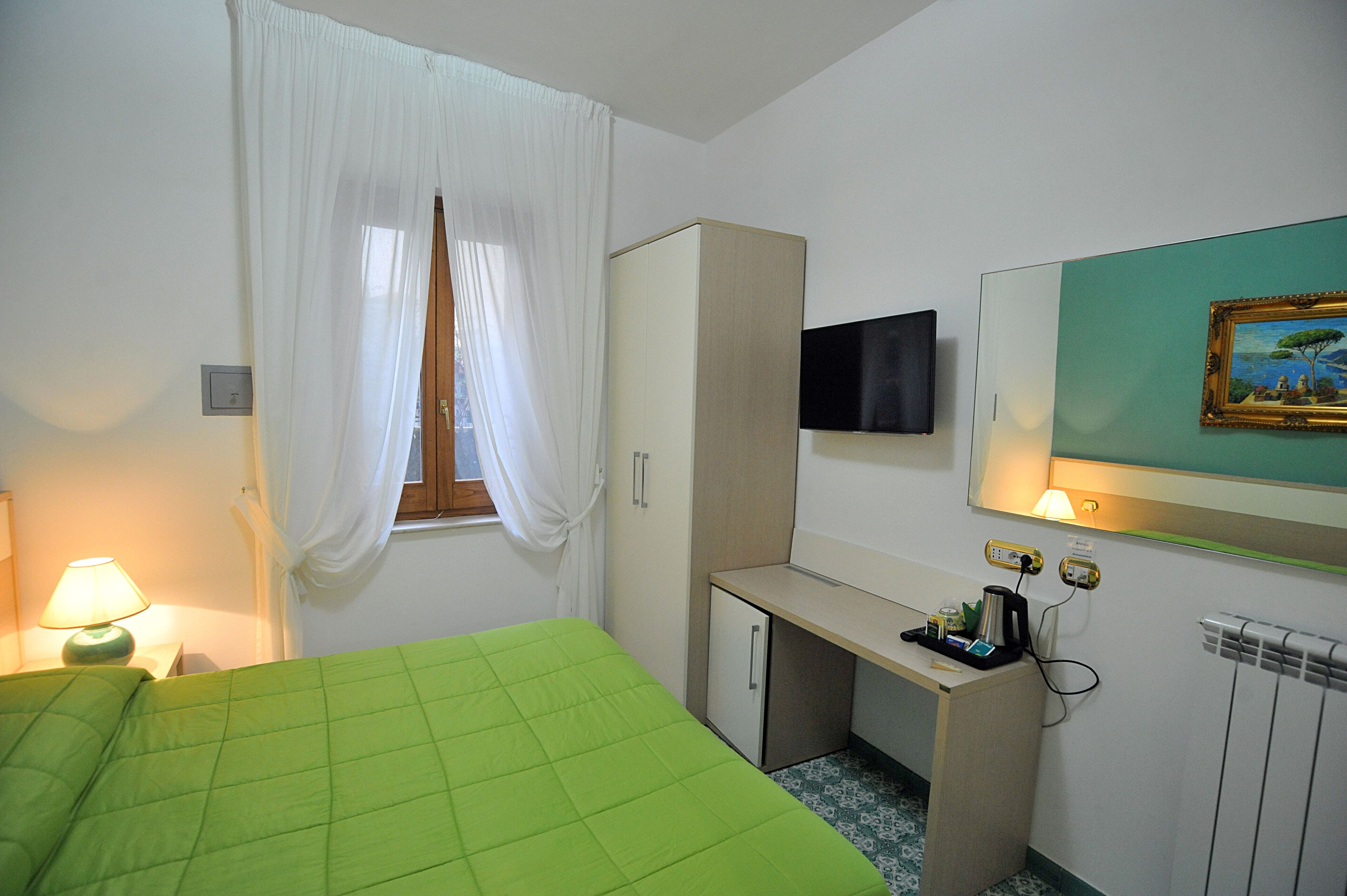 A hotel room with a bed, a desk, a TV, and a painting on the wall.