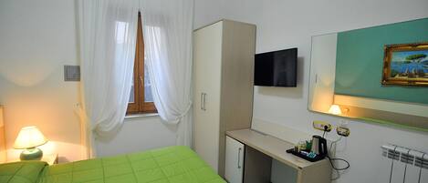 A hotel room with a bed, a desk, a TV, and a painting on the wall.