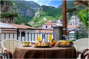 A table set with breakfast items, including croissants, fruit, and juice, overlooking a mountainous village with traditional buildings. - Villa Adriana B&B (Amalfi)