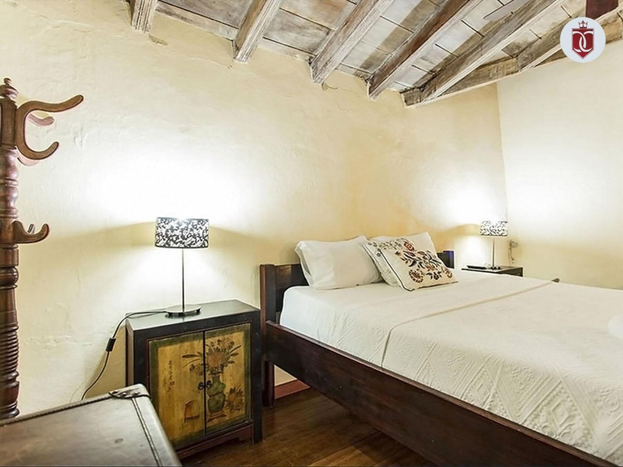 A bedroom with a wooden bed, a nightstand with a lamp, and a cabinet with a floral design.