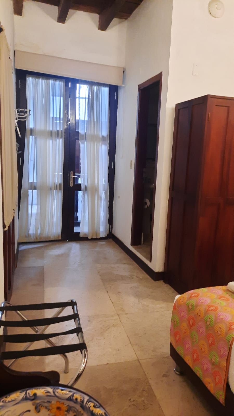 A room with a bed, a chair, a wooden wardrobe, and a door leading to another room.
