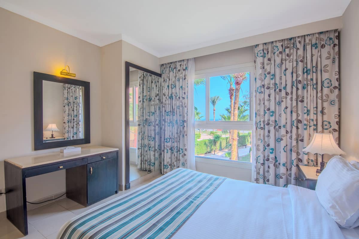 A hotel room with a bed, a desk, a mirror, and a window with curtains.