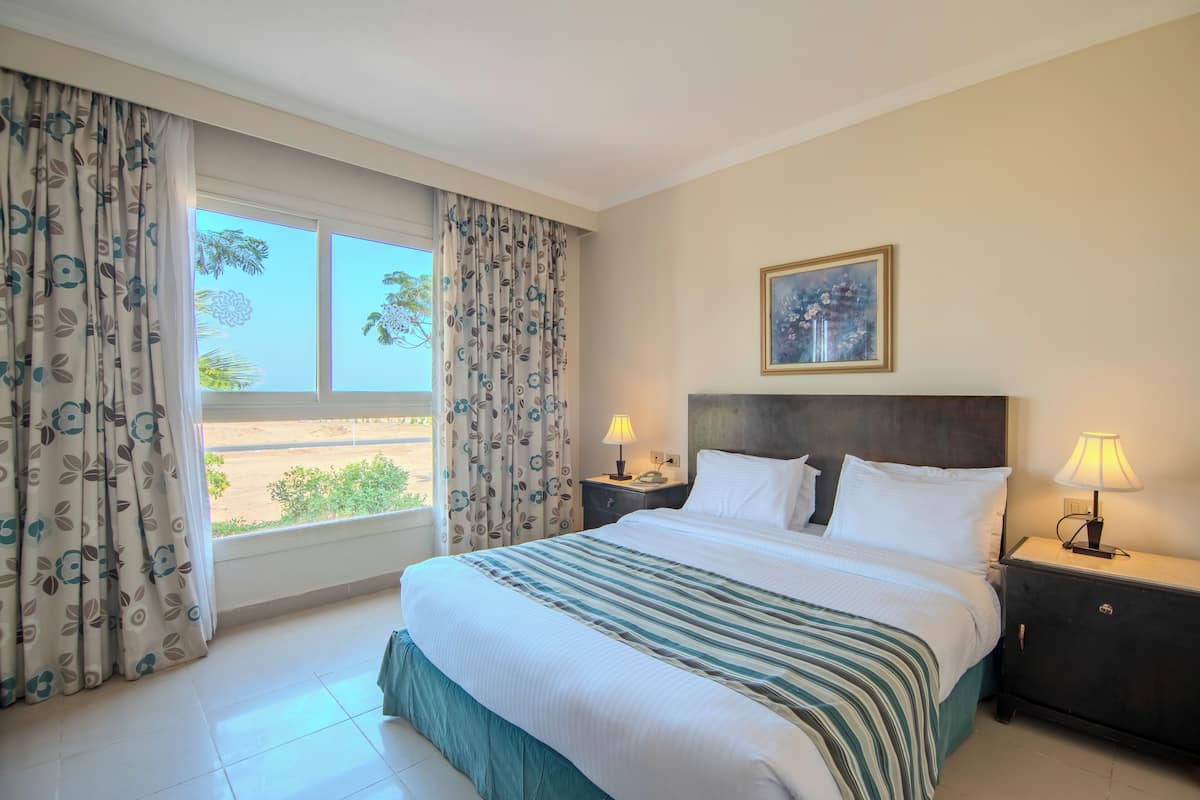 A hotel room with a large bed, two bedside tables with lamps, a window with curtains, and a framed picture on the wall.