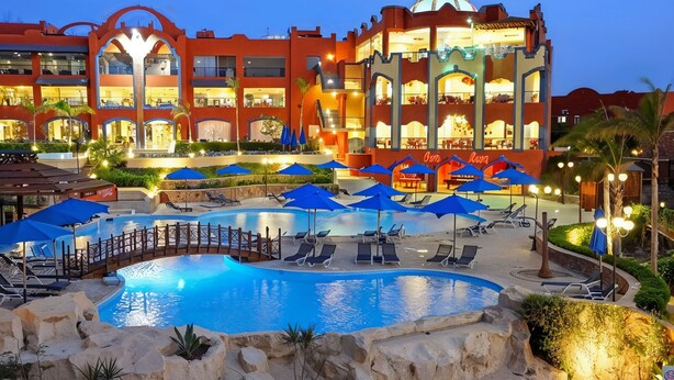 Un hotel con una piscina grande, varias opciones de restauración y zonas de estar al aire libre con sombrillas.