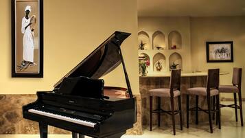 Un piano de cola en una habitación bien iluminada con una zona de comedor que incluye sillas de madera y una encimera de mármol.