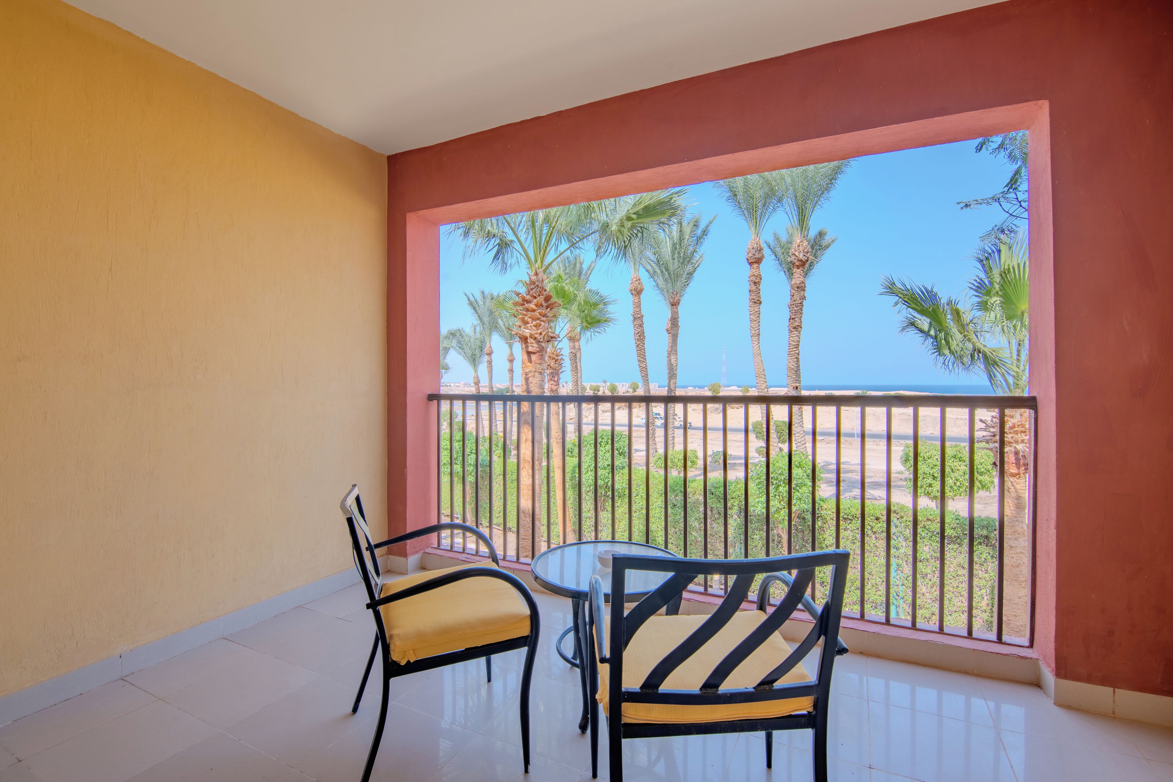 Un balcon avec deux chaises et une table, offrant une vue sur un paysage bordé de palmiers.