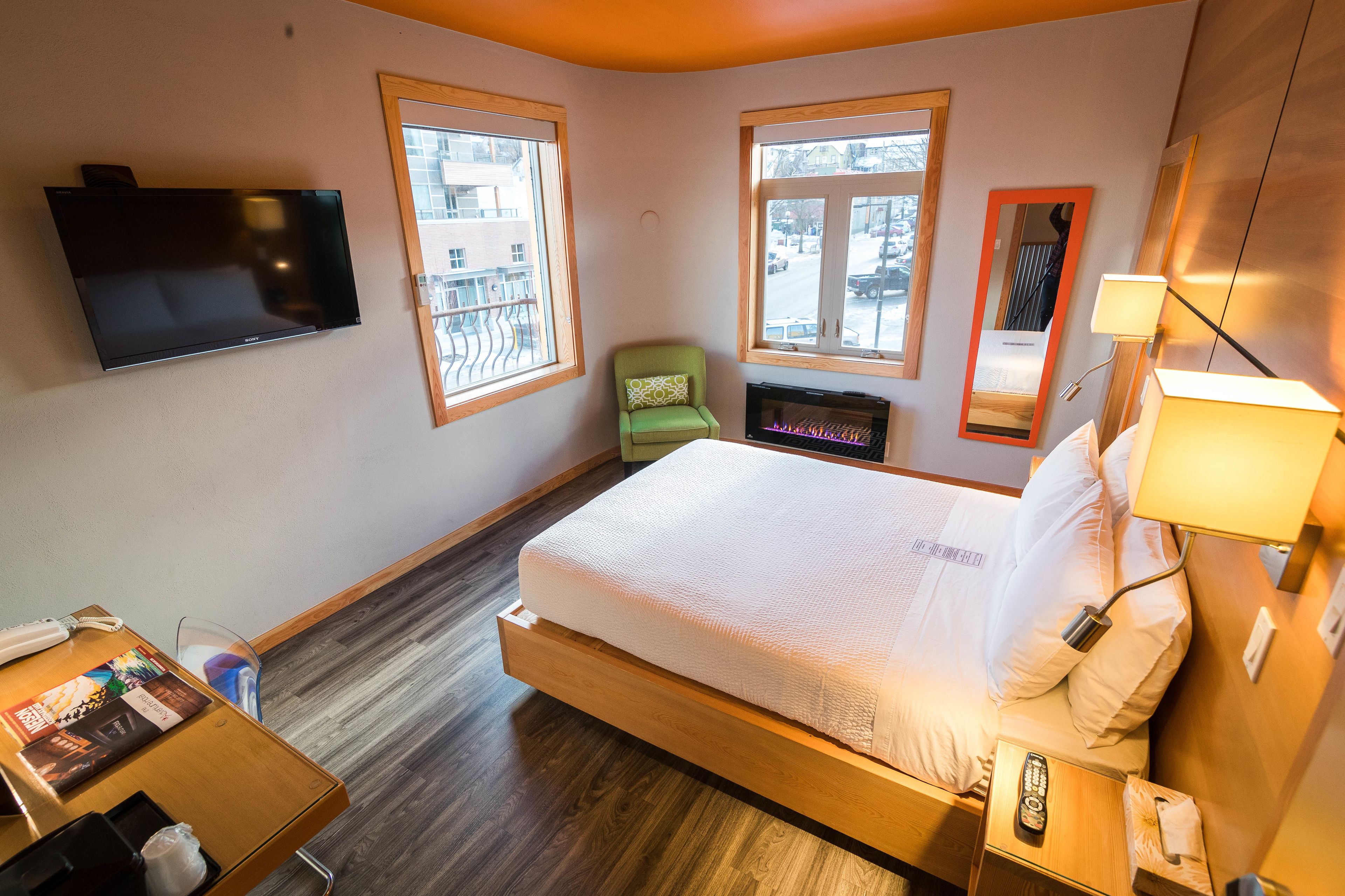 Una habitación de hotel con cama, mesita de noche, lámpara, televisor y ventanas.