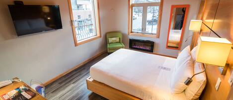 Una habitación de hotel con cama, mesita de noche, lámpara, televisor y ventanas.
