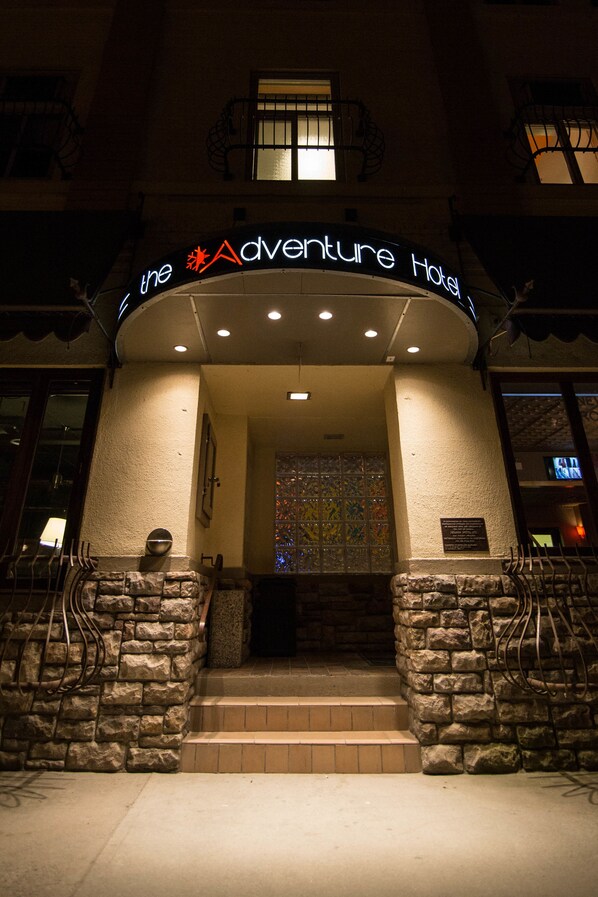 The exterior of the Adventure Hotel with a stone facade, a large glass window, and a sign above the entrance.