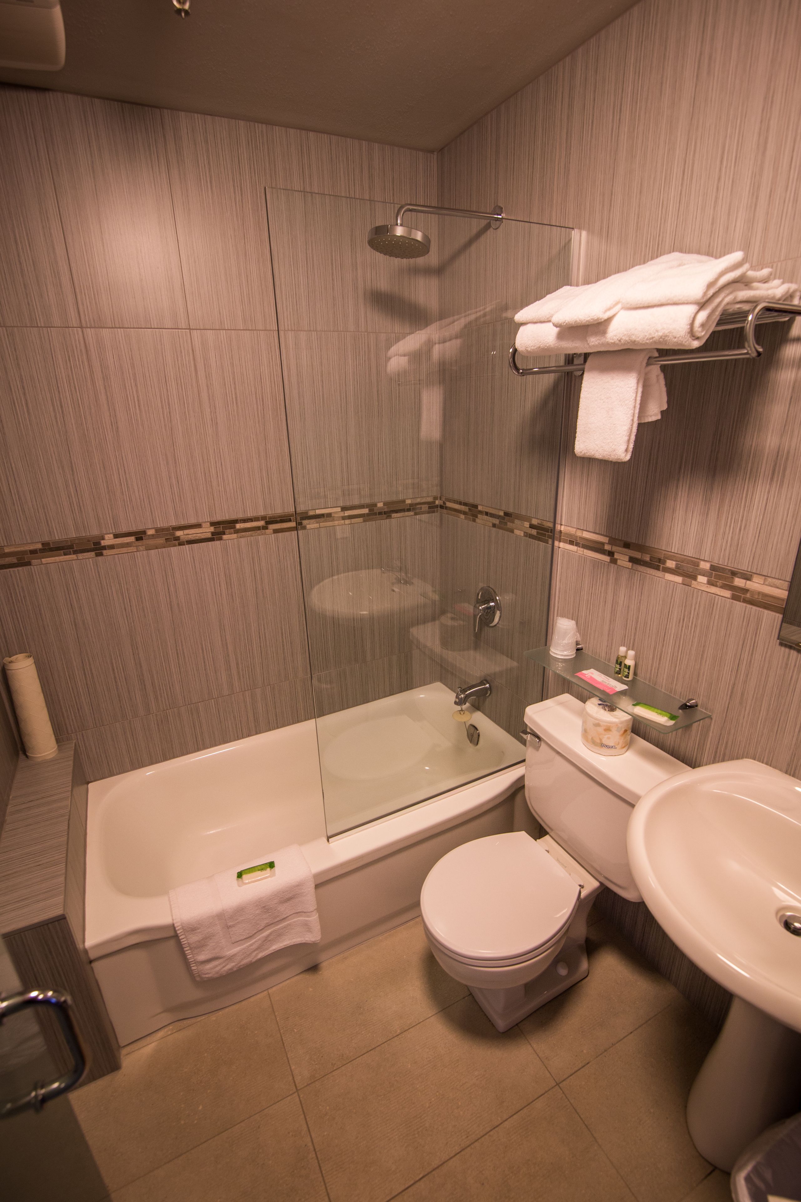 Un baño con ducha envuelta en vidrio, un inodoro, un lavamanos y un perchero con toallas dobladas.