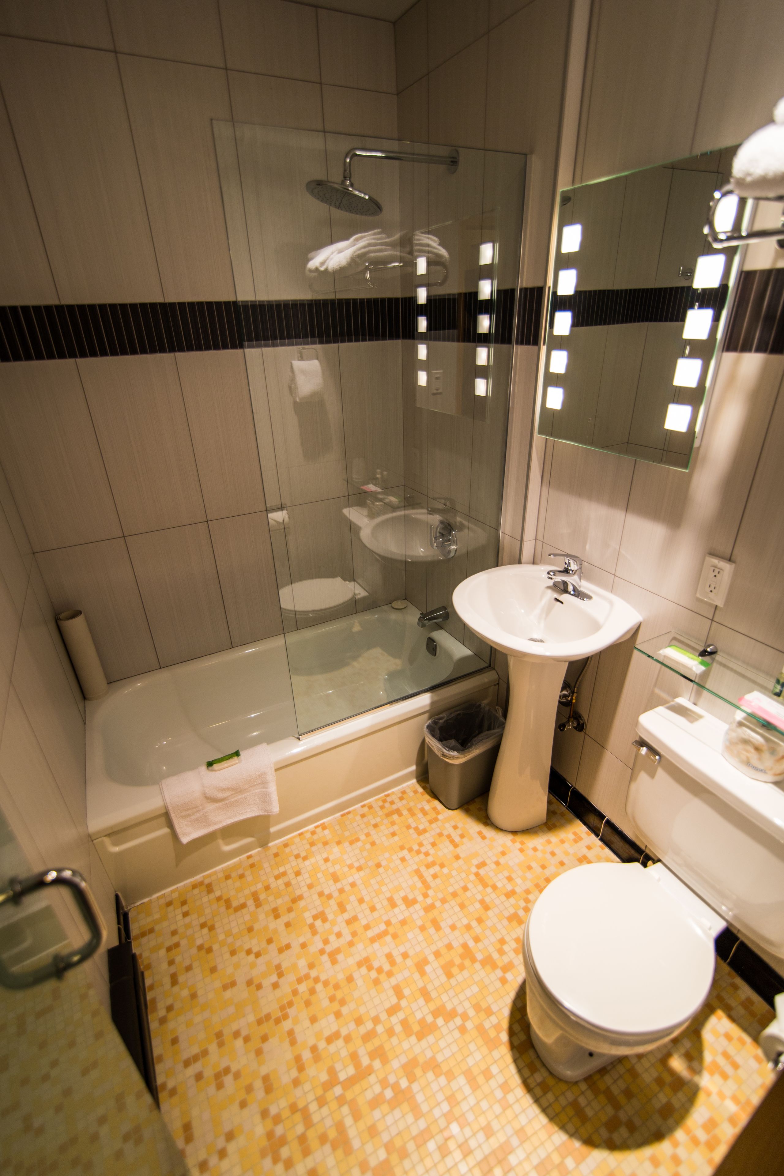 A modern bathroom with a glass-enclosed shower, a pedestal sink, and a toilet.