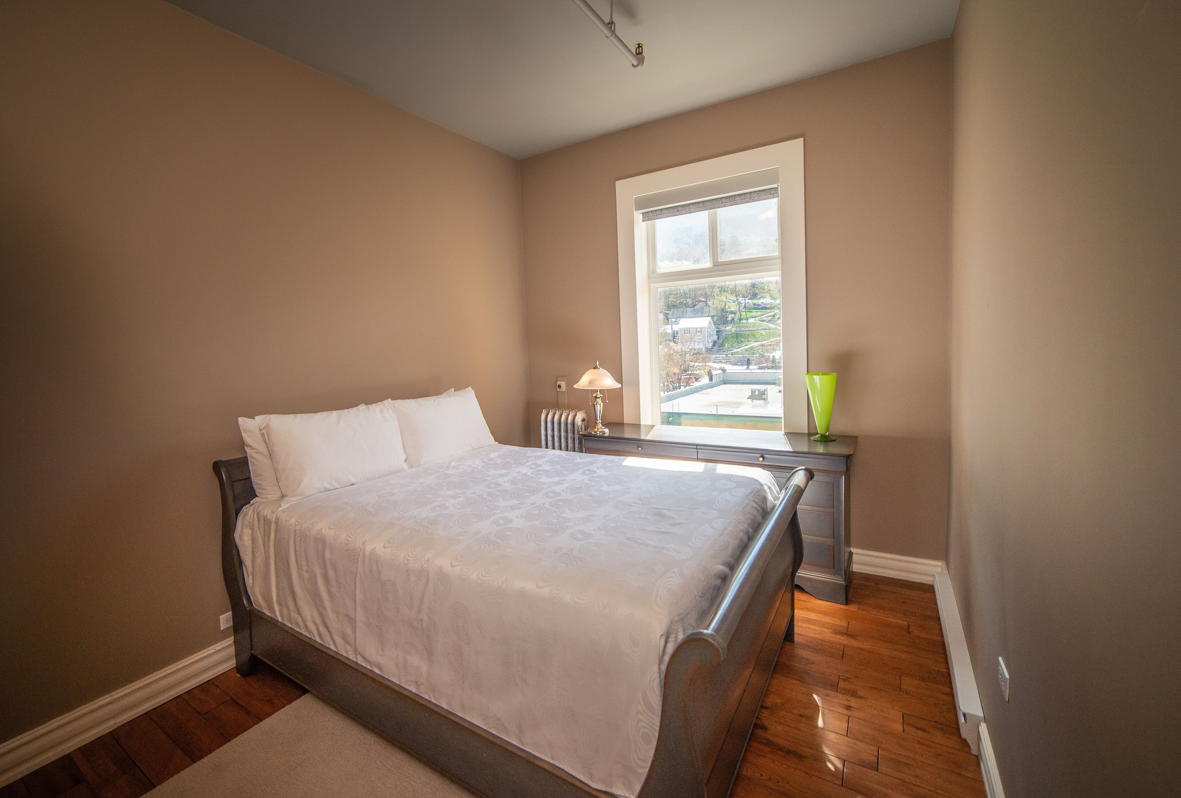 A bedroom with a bed, a window, a nightstand, and a lamp.