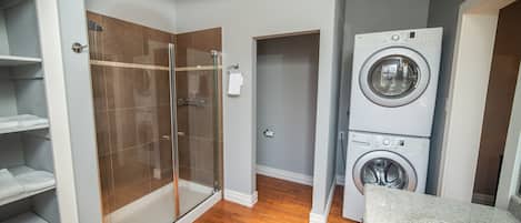 A compact bathroom with a glass shower enclosure, a stacked washer and dryer, and a built-in sink.