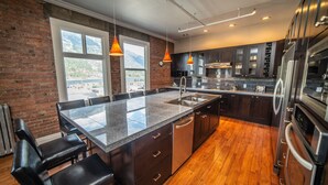 A modern kitchen with a large island, dark cabinetry, and stainless steel appliances. - The Adventure Hotel (Nelson)