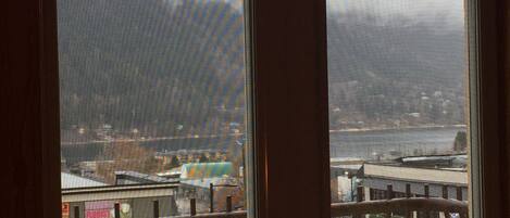 A view through a window with a metal railing, overlooking a street with buildings and a hilly landscape in the distance.