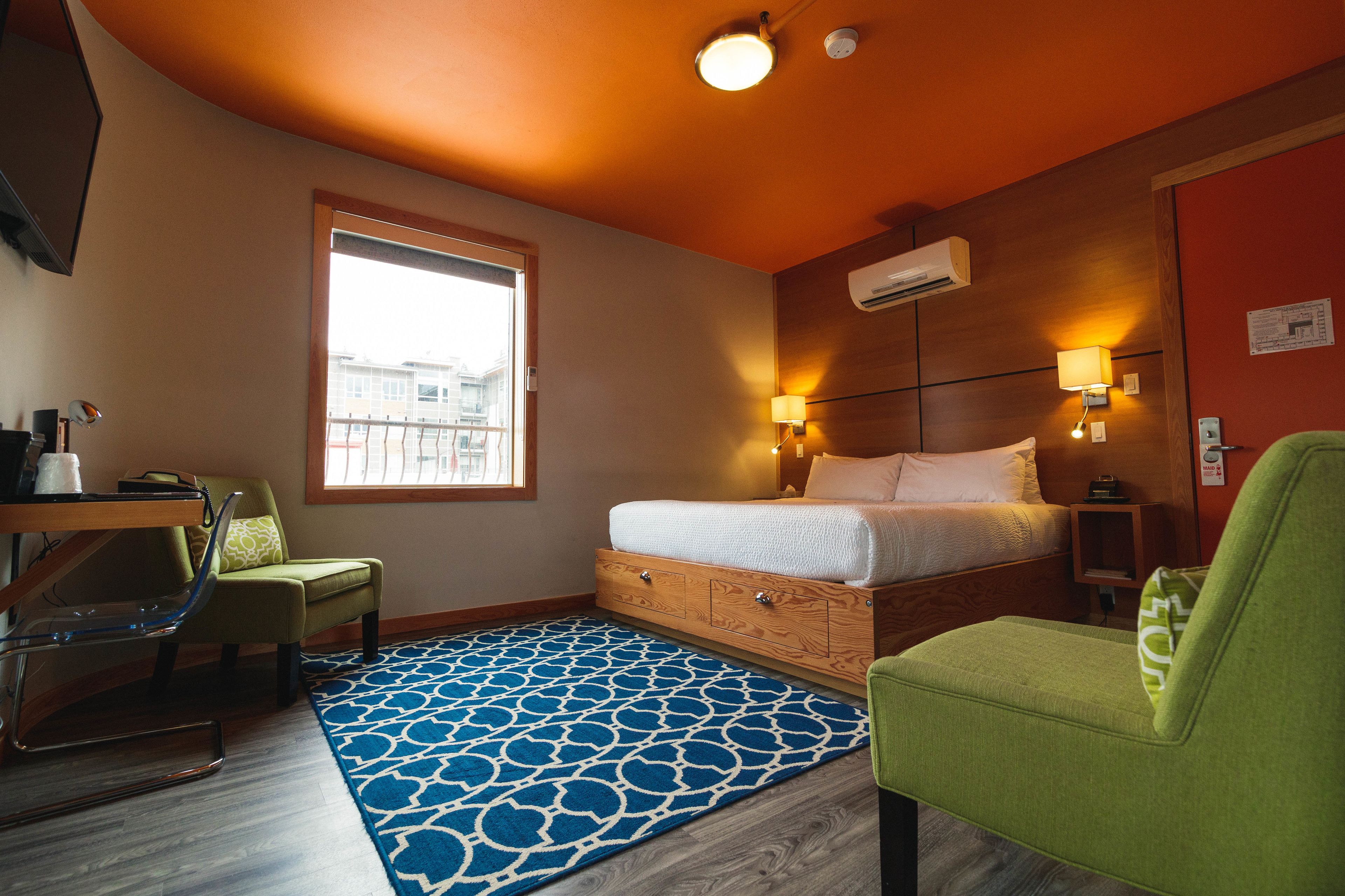 Ein Hotelzimmer mit einem Bett, einem Schreibtisch, einem Stuhl, einem Fenster und einem gemusterten Teppich.