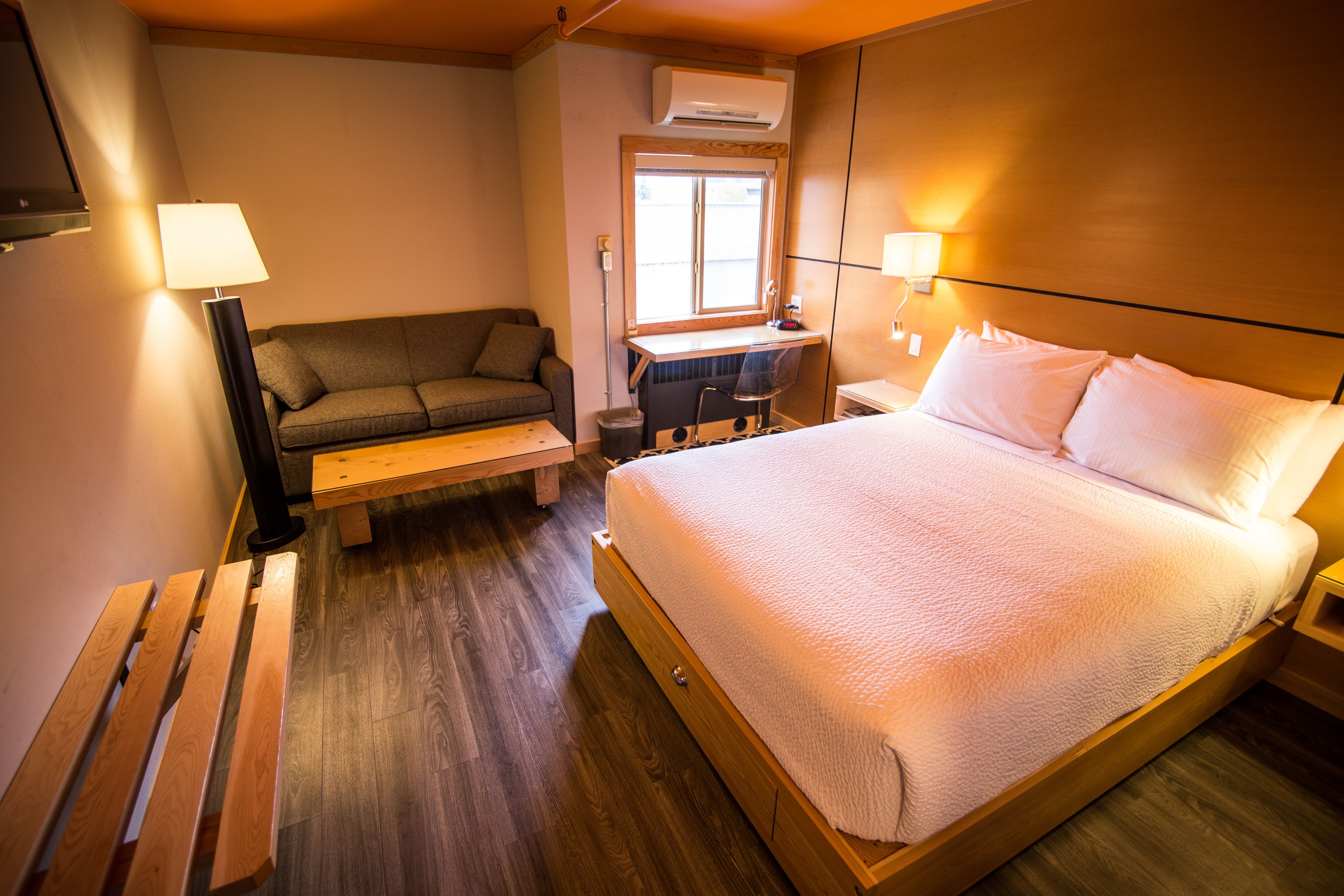 A hotel room with a large bed, a desk, a chair, a sofa, and a lamp.