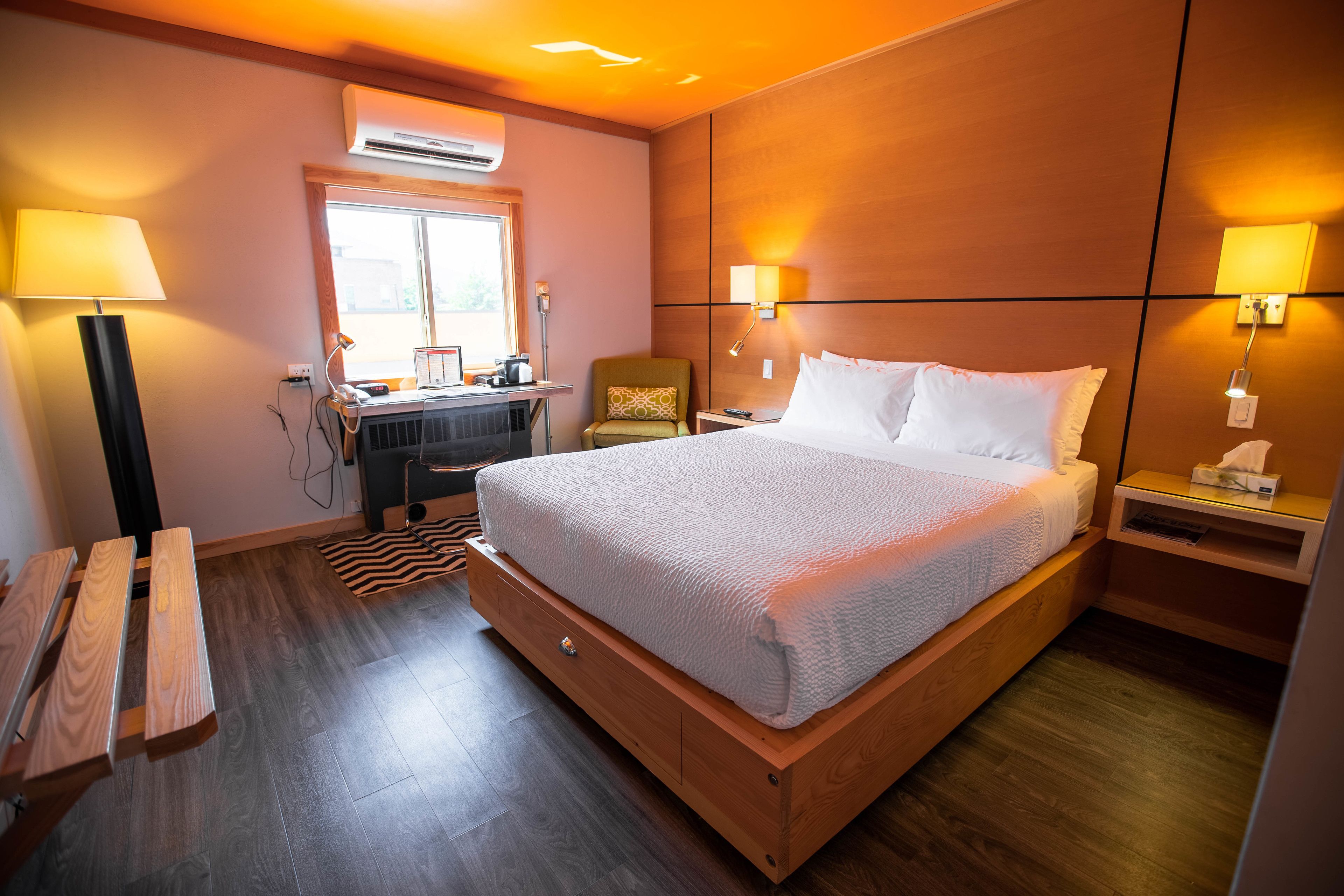 A hotel room with a wooden bed, bedside tables, a desk with a chair, and a window.