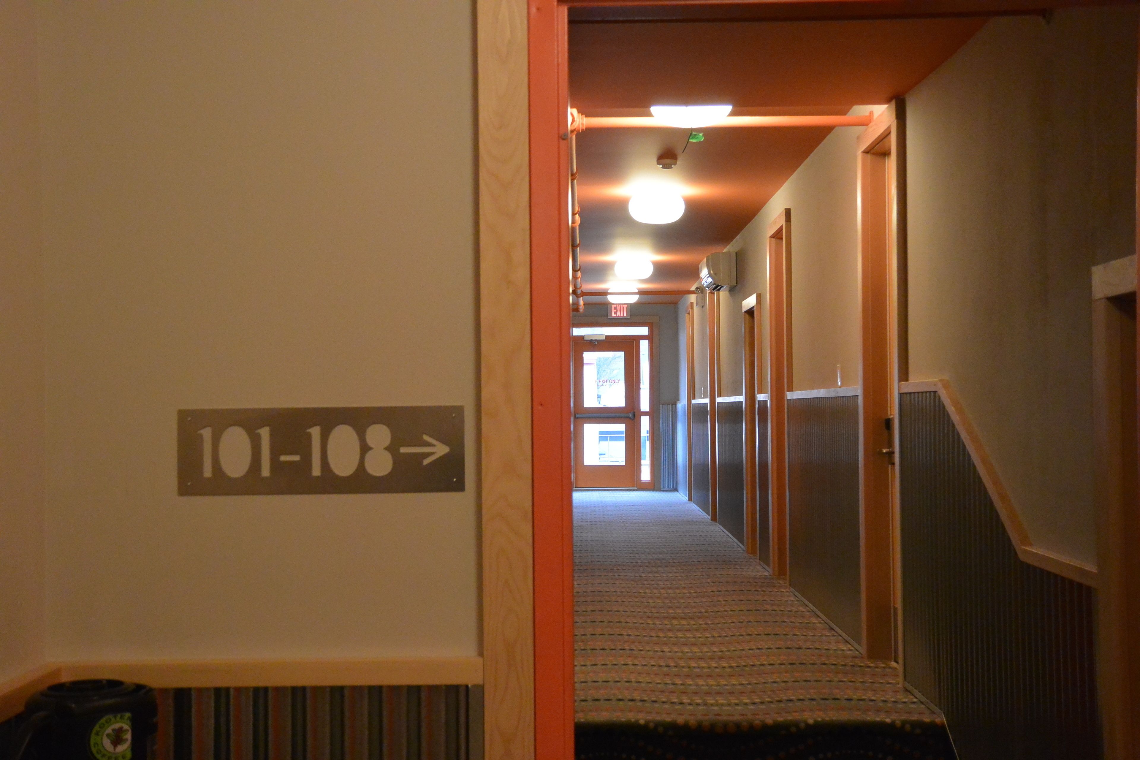 Un pasillo de hotel con piso alfombrado, puertas de madera y un cartel que indica las habitaciones 101 a 108.