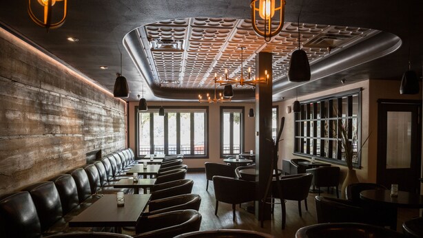A restaurant with a long bench seating area, tables, and a modern ceiling design. - The Adventure Hotel (Nelson)