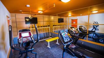 Un gimnasio con equipo de ejercicio, una televisión y un espejo.
