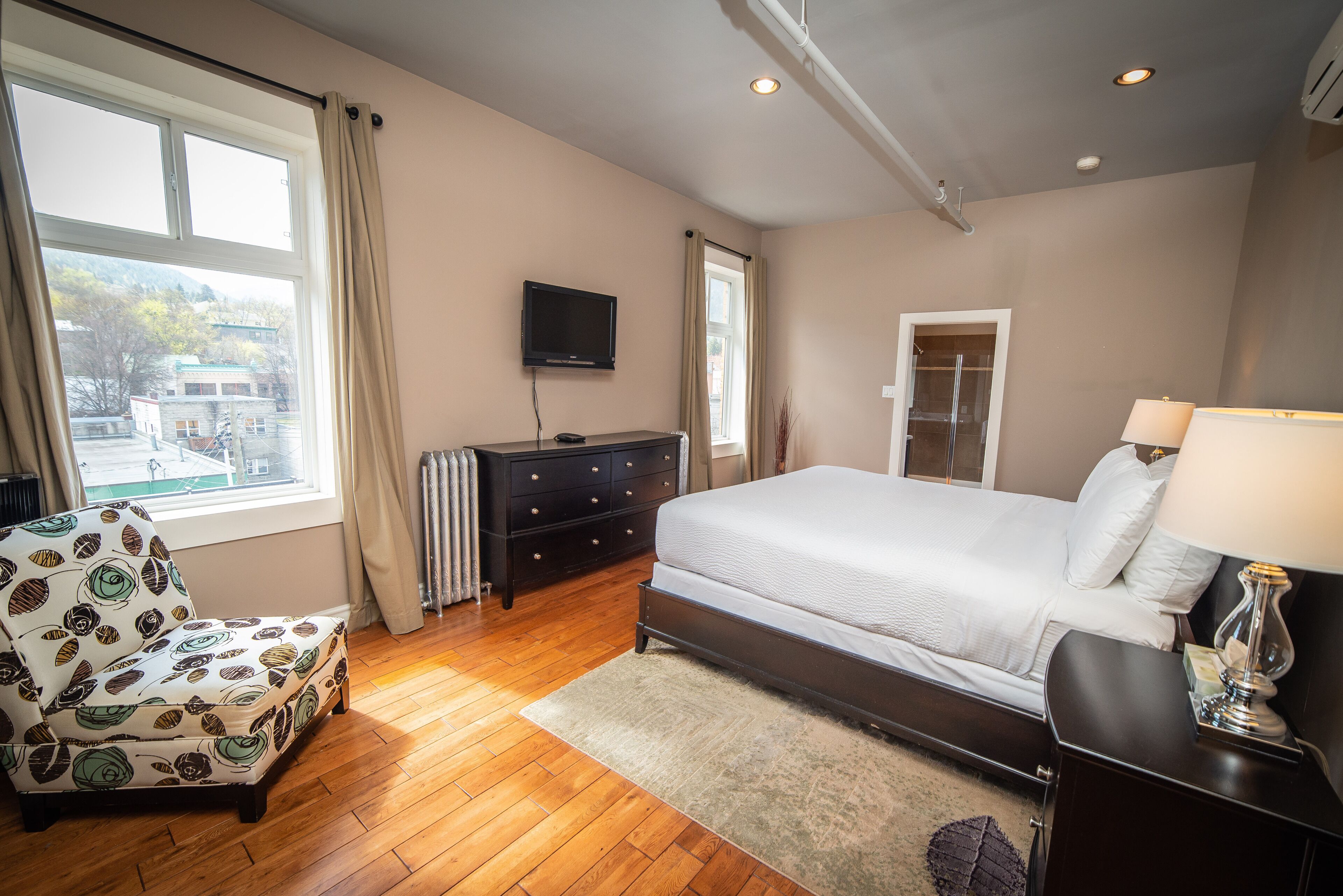 A bedroom with a bed, a chair, a dresser, a TV, and a window with curtains.