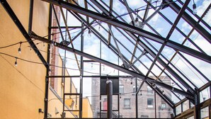 An indoor patio with wooden tables and red chairs, a glass ceiling, and a view of the cityscape. - The Adventure Hotel (Nelson)