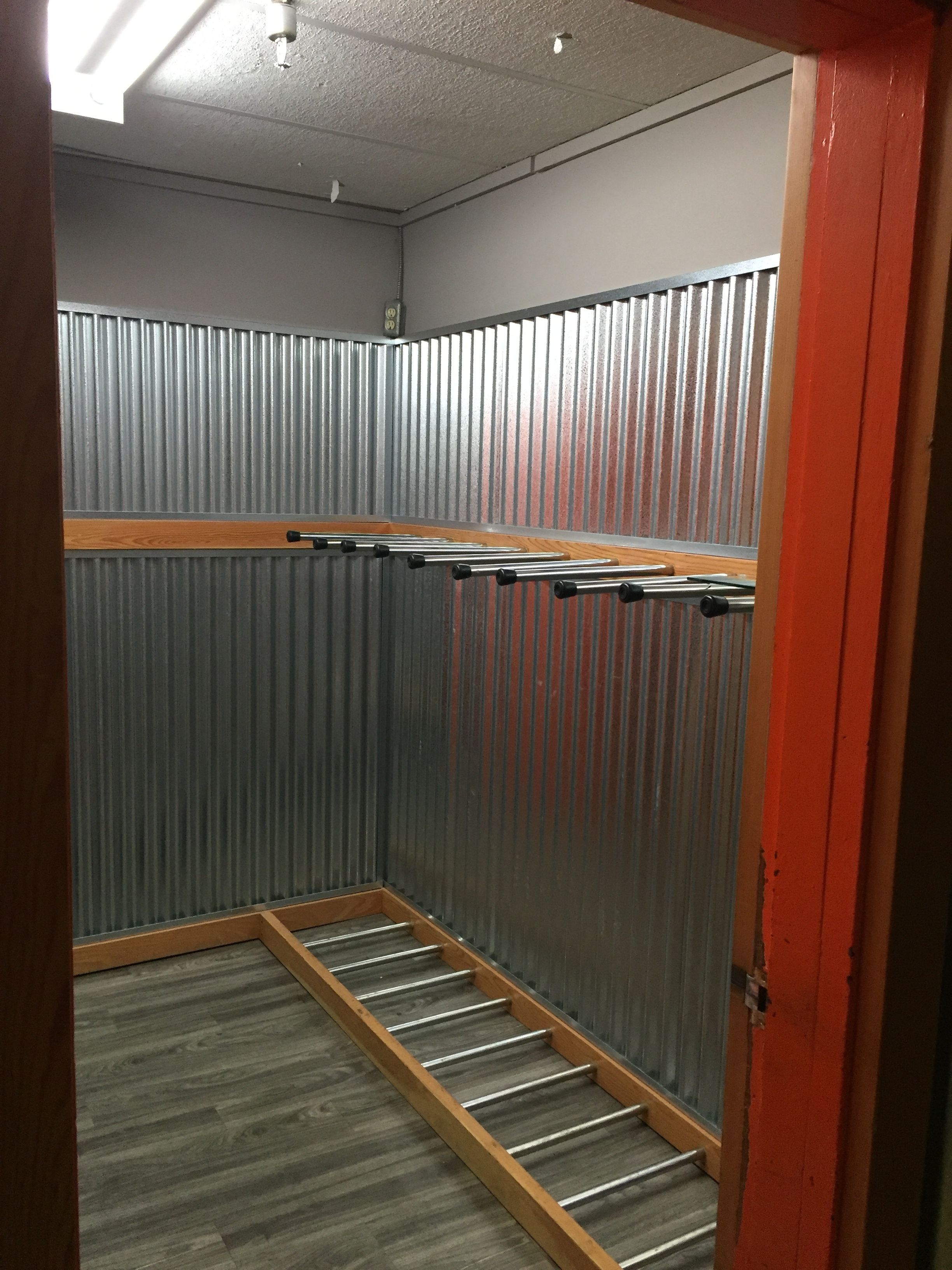 Una habitación con pared de metal, suelo de madera y una estantería metálica.
