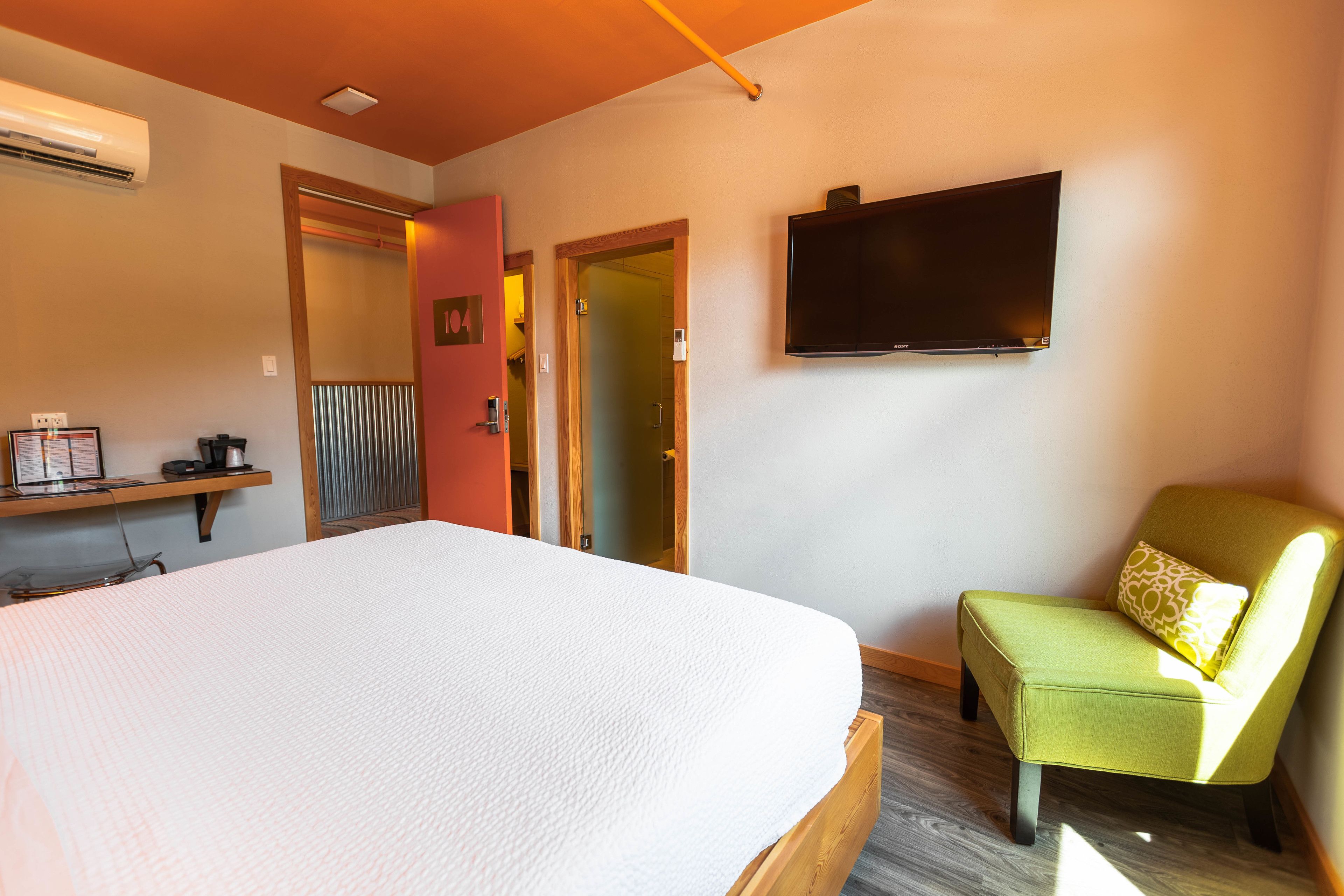A hotel room with a large bed, a television mounted on the wall, a green armchair, and a wooden floor.