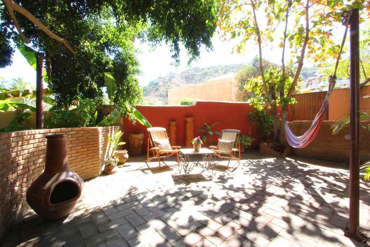 Eine Terrasse mit Backsteinboden, zwei Korbstühle, einem Tisch und einer Hängematte.