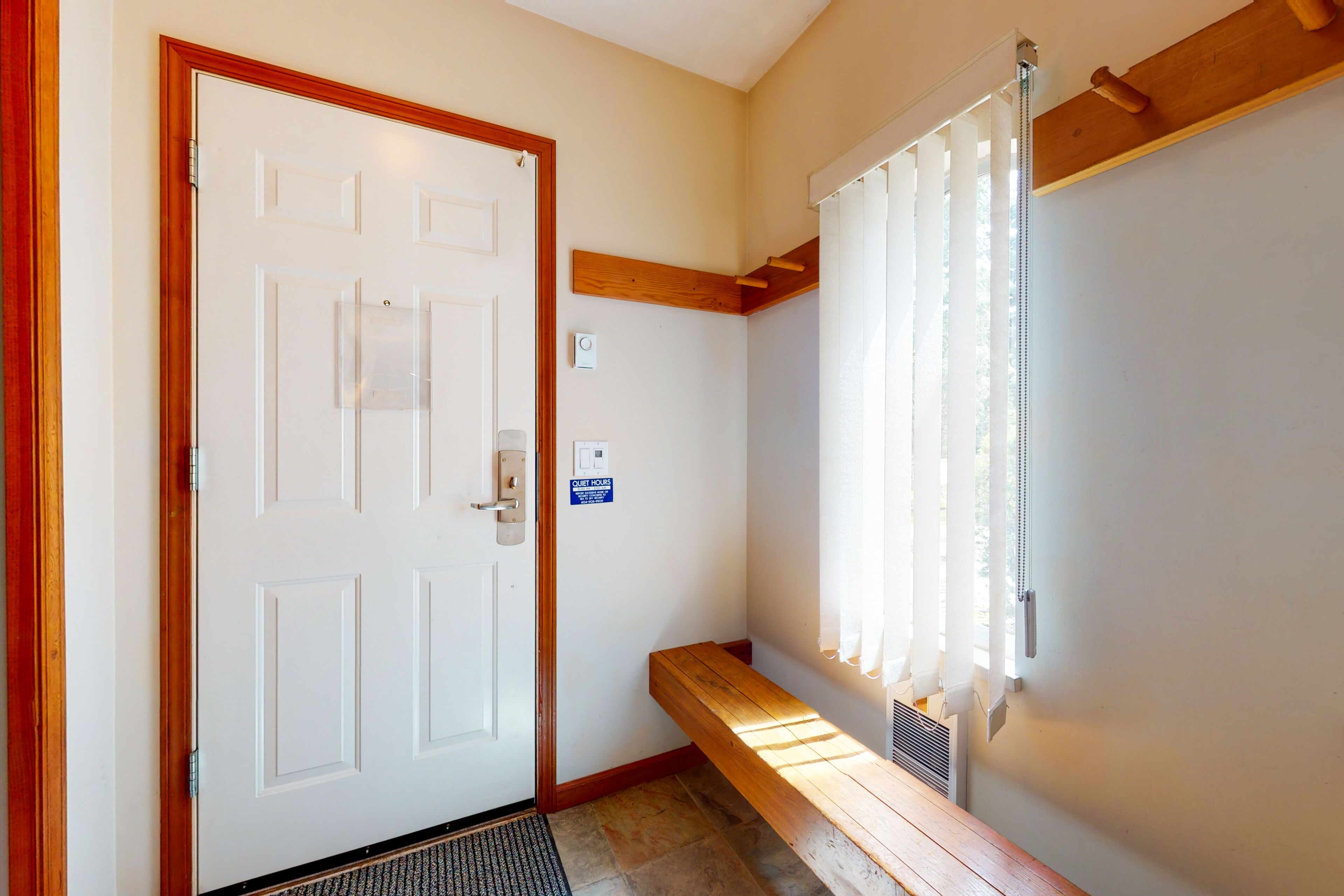 A door with a handle, a bench, a window with blinds, and a thermostat on the wall.