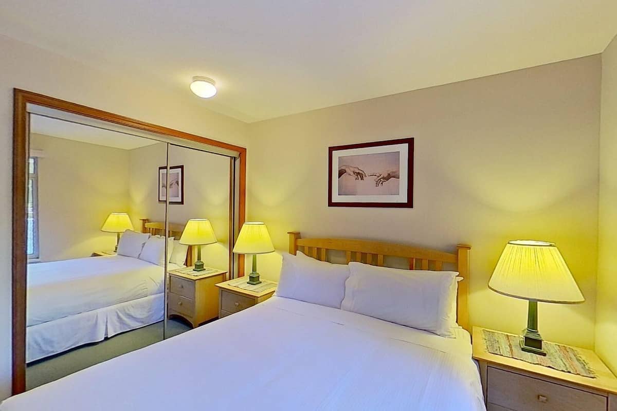 Ein Hotelzimmer mit einem großen Bett, zwei Nachttischen mit Lampen, einem Spiegel, einem gerahmten Bild an der Wand und einer Deckenleuchte.