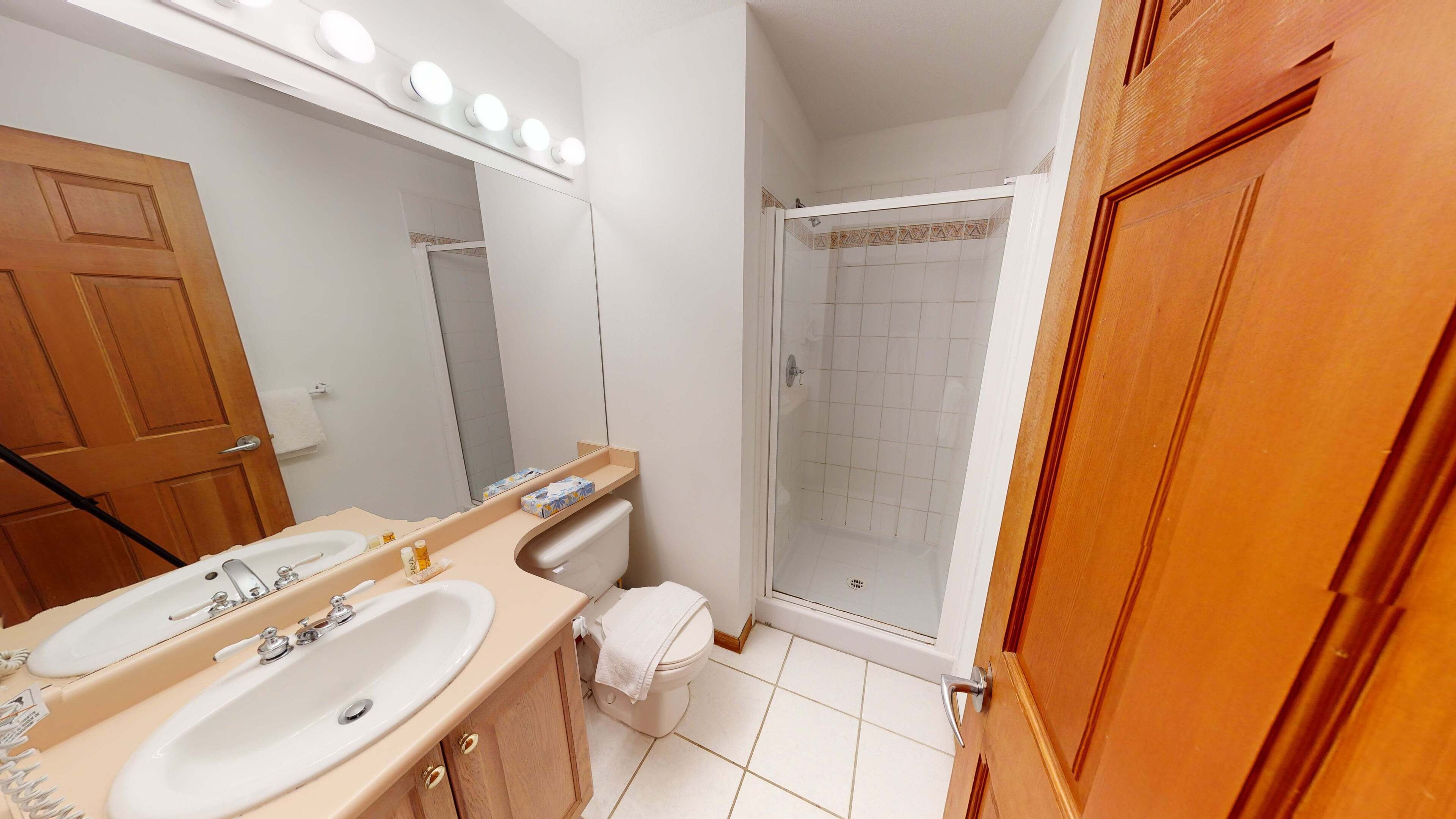 Un baño con dos lavamanos, un espejo, una ducha y puertas de madera.