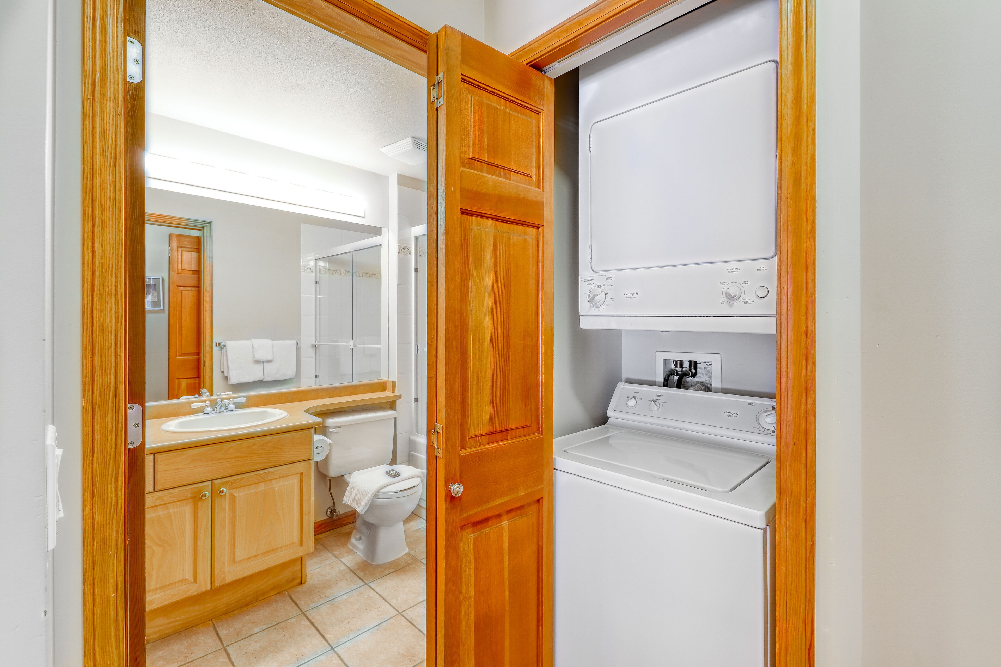 Une salle de bain avec un meuble-lavabo en bois, des toilettes et un lave-linge et un sèche-linge superposés.