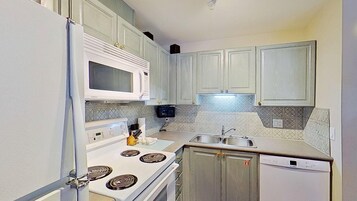Una cocina compacta con electrodomésticos blancos, microondas, estufa y lavavajillas.