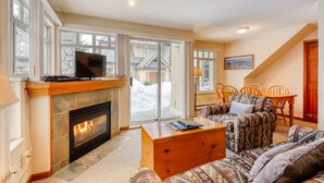 A living room with a fireplace, a television, a sofa, a coffee table, and a dining area with chairs. - Stoney Creek Lagoon - Whistler Premier (Whistler)