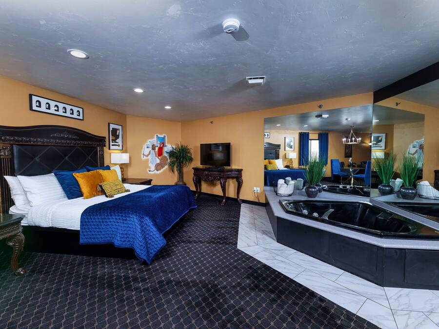 A hotel room with a large bed, a sitting area with a sofa and a coffee table, a bathtub, and a large mirror.