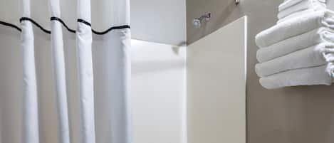 Et badeværelse med bruseforhæng, badekar, toilet og en stak håndklæder.