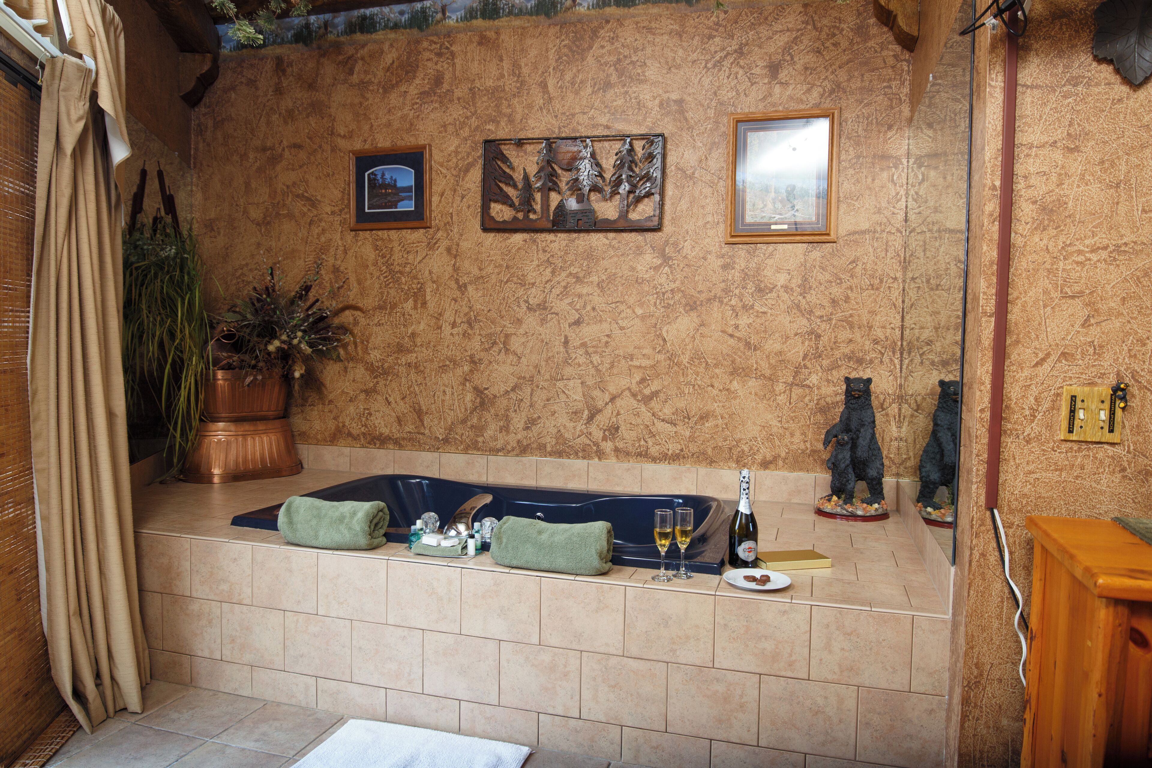 A bathroom with a bathtub, two framed pictures, a potted plant, and a bottle of champagne.