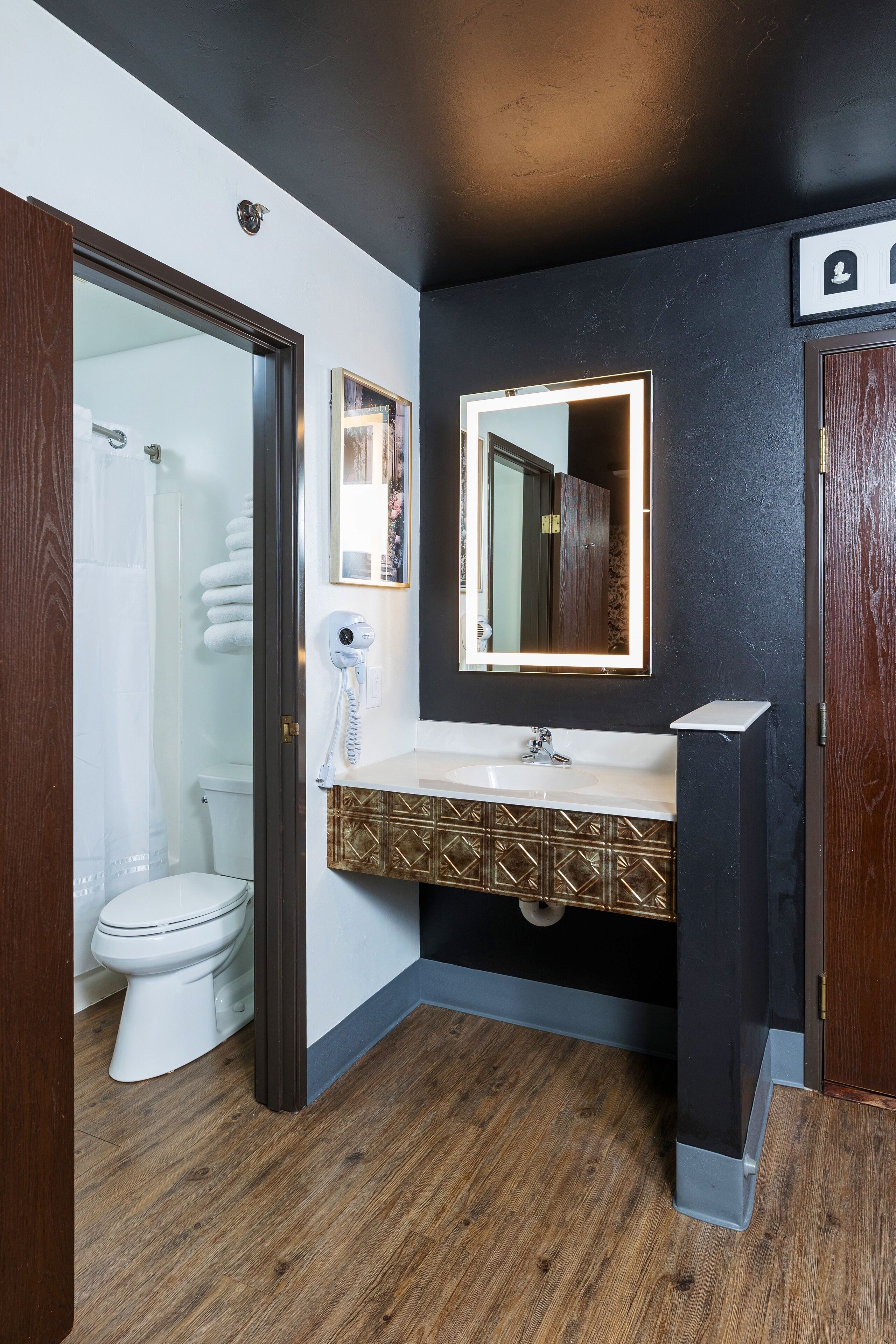 Un baño moderno con inodoro blanco, cabina de ducha de vidrio, tocador con mueble estampado en dorado y espejo con marco iluminado.
