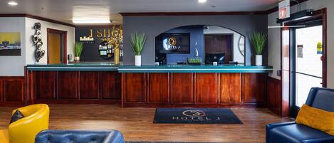 A hotel reception area with a counter, seating, and a TV screen displaying the hotel name.