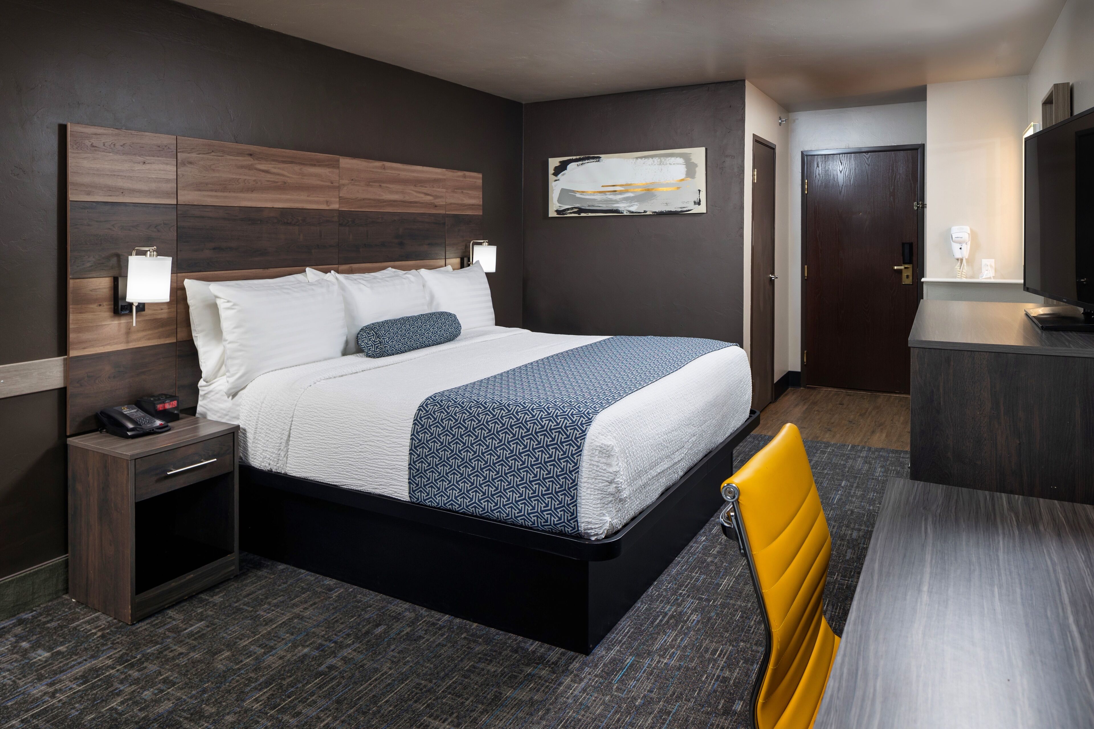 A hotel room with a bed, bedside table, chair, and a desk with a chair.